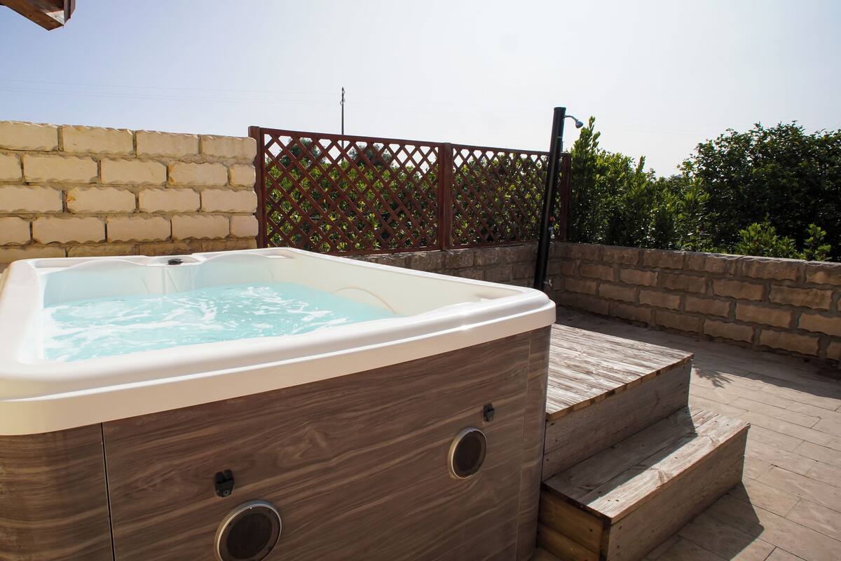Un bain à remous sur une terrasse en bois, avec un mur en briques et une clôture en treillis au fond.