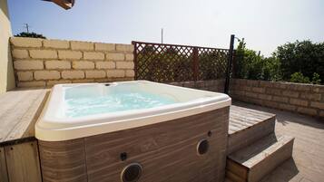 Un jacuzzi en una terraza de madera, con una pared de ladrillo y una valla de celosía al fondo.