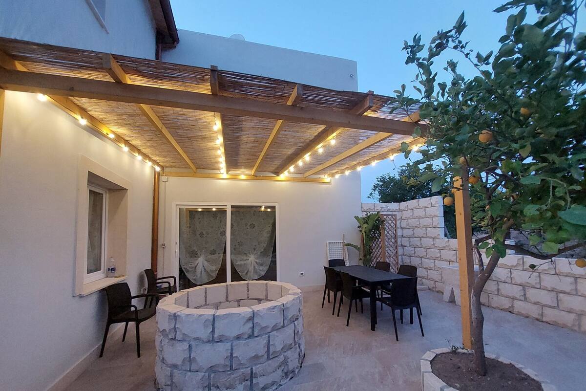 Un espace extérieur aménagé, abrité, avec un foyer en pierre, des chaises et une table.