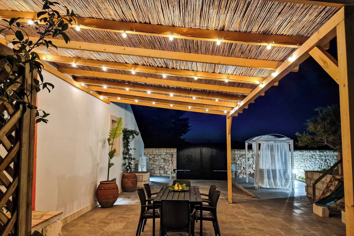 Une terrasse extérieure dotée d’une pergola en bois, d’un mur en pierre et d’un espace salon abrité.