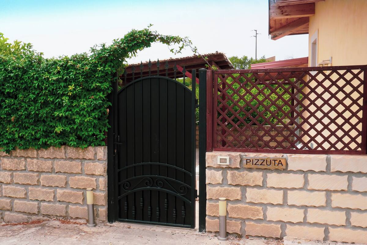Une entrée fermée par un portail, avec un mur en briques et une enseigne indiquant « PIZZUTA ».