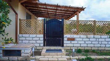 A black gate with a metal handle, a wooden nameplate reading "BAIA", and a stone wall with a tiled roof structure.