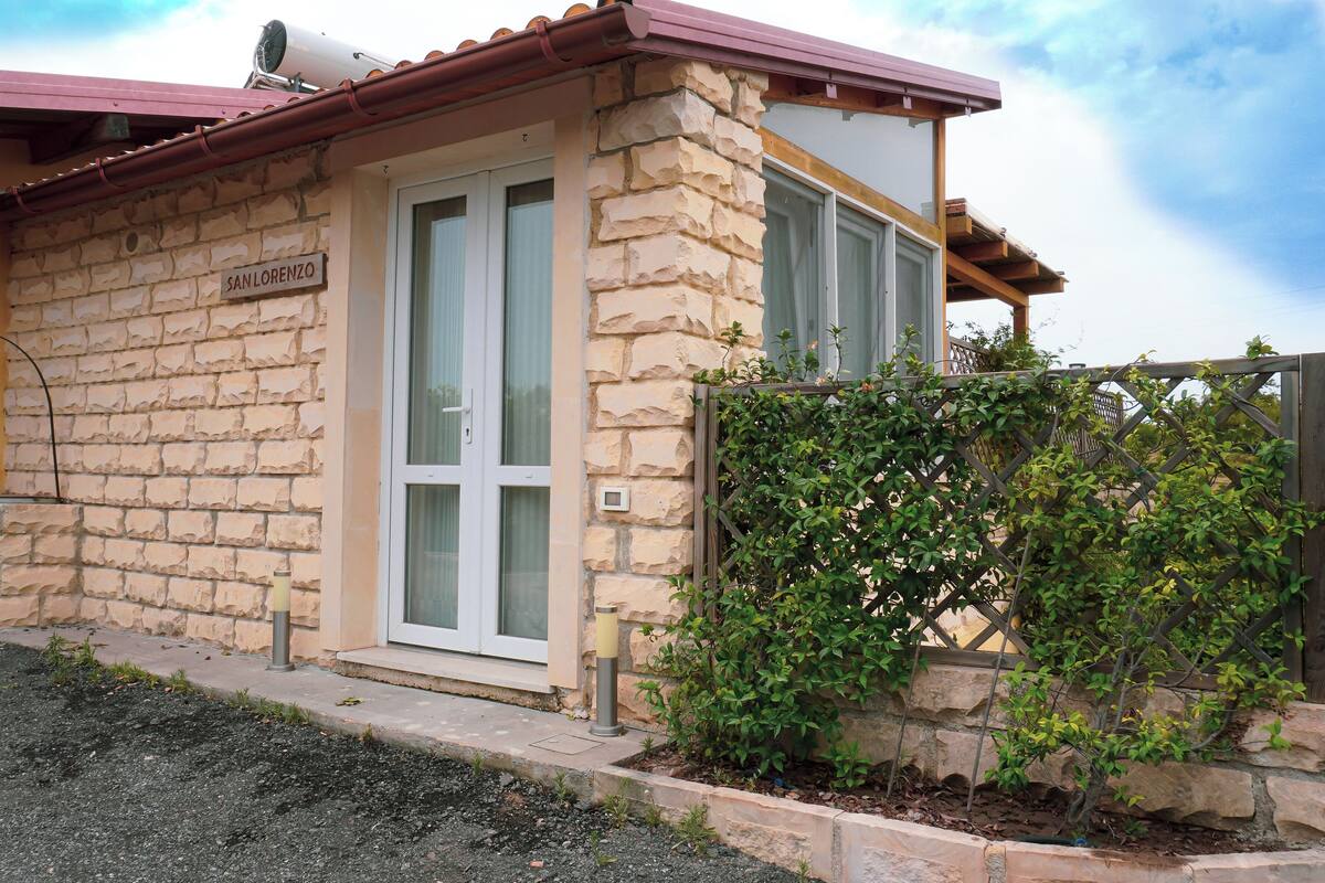 Un bâtiment en pierre avec une enseigne indiquant « SAN LORENZO », une porte et un petit jardin agrémenté de plantes.