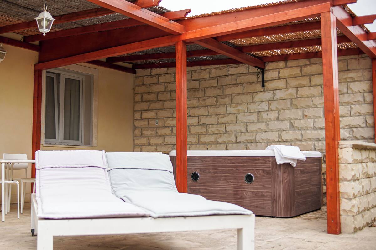 Une pièce avec un lit, un bain à remous en bois, un mur en pierre et une fenêtre.