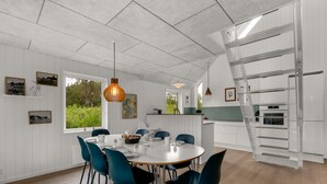 Una cucina moderna con mobili bianchi, un'area pranzo con un tavolo rotondo e sedie color petrolio, e vista sul verde circostante.