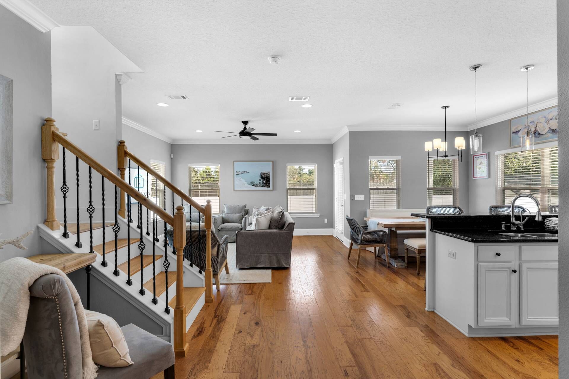 Amplia sala de estar con una escalera de madera, un sofá gris y un comedor con isla de cocina.