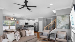 A modern living room with a sofa, chairs, a dining area, kitchen, and a staircase.