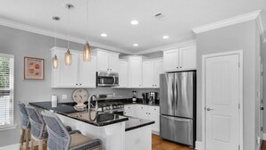 A modern kitchen with white cabinetry, stainless steel appliances, a central island with bar stools, and pendant lighting.