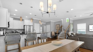 A modern kitchen with white cabinets, stainless steel appliances, and a dining area with a wooden table and wicker chairs.