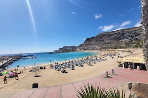 A beach with a rocky cliff, palm trees, and a sign for Palm Beach. - House in Mogán near Playa de Amadores (Mogán)