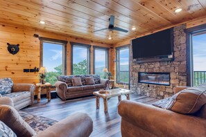 A cozy cabin interior with wooden walls, a stone fireplace, a large TV, and a sofa set.