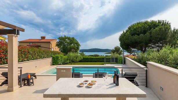 A poolside area with a table set for dining, a pool, and a view of a lake and hills. - Villa Kliman by Villas Guide (Medulin)