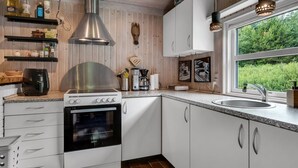 A modern kitchen with white cabinets, a stainless steel range hood, a built-in oven, and a window providing a view of greenery. - "Ginette" - 400m to the fjord by Interhome (Aabybro)