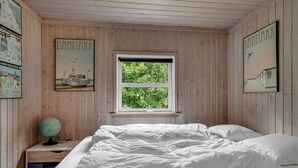 A bedroom with a wooden paneled wall, a window with a view of greenery, a bed with white bedding, and a globe on a nightstand. - "Ginette" - 400m to the fjord by Interhome (Aabybro)