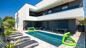 Een modern gebouw met twee verdiepingen, een zwembad, terras en een overdekte patio.