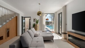 A modern living room with a grey sectional sofa, a flat-screen TV, and a pool view. - Vila Laguna Blu by Villas Guide (Trget)
