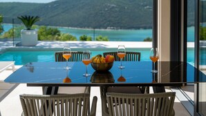 A dining table with a fruit bowl and glasses, overlooking a pool and a scenic view. - Vila Laguna Blu by Villas Guide (Trget)