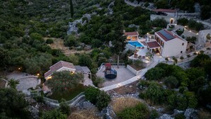 An aerial view of a property with a swimming pool, outdoor seating, and a staircase leading to a building with a red roof.