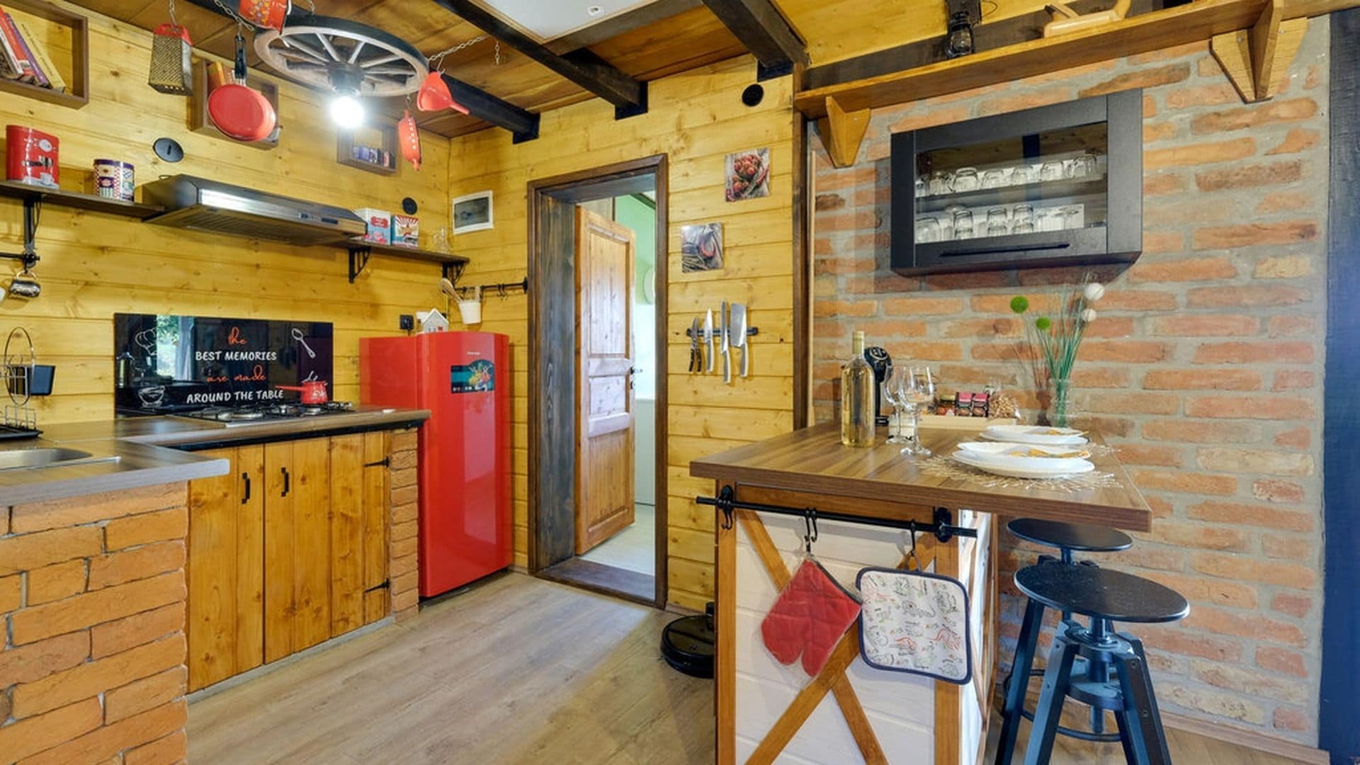 A rustic kitchen with wooden walls, a red refrigerator, and a dining area with stools.
