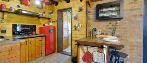 A rustic kitchen with wooden walls, a red refrigerator, and a dining area with stools.