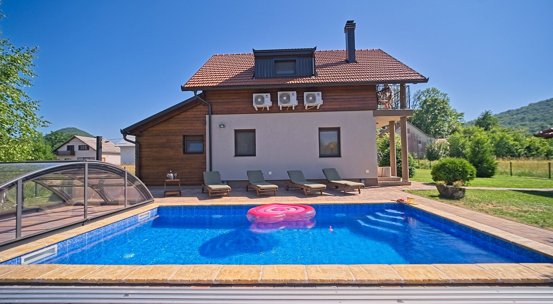 A two-story house with a swimming pool, outdoor seating, and air conditioning units.