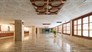 Un corredor amplio con piso de mármol pulido, ventanas grandes a un lado y techo con diseño.