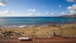 Una playa con agua azul cristalina, orilla de arena y algunas personas.
