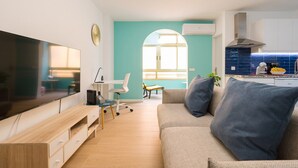 Una sala moderna con una televisión de pantalla plana, un mueble bajo de madera, un sofá color beige y un escritorio pequeño con una silla.