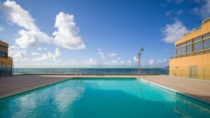 Una piscina con agua cristalina azul, rodeada por una terraza y con vistas al océano.