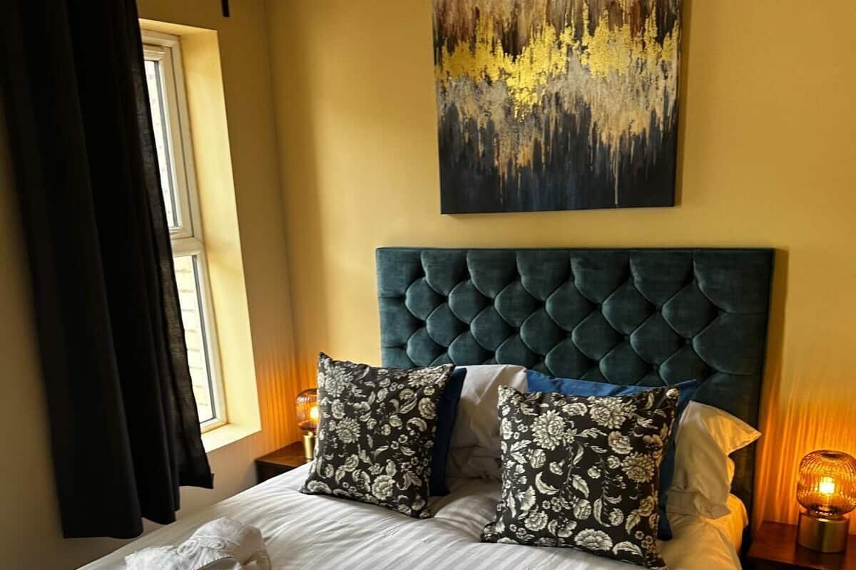 A neatly made bed with two pillows, a headboard, and a painting above it.