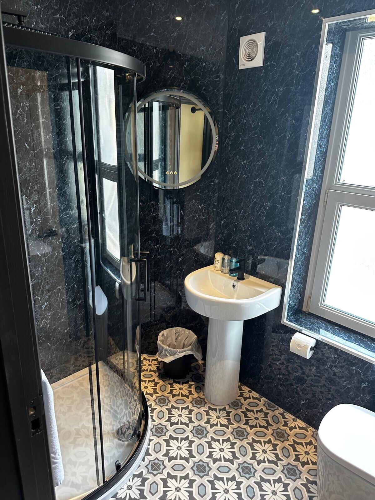 Un baño con cabina de ducha de vidrio, lavamanos pedestal y piso estampado.