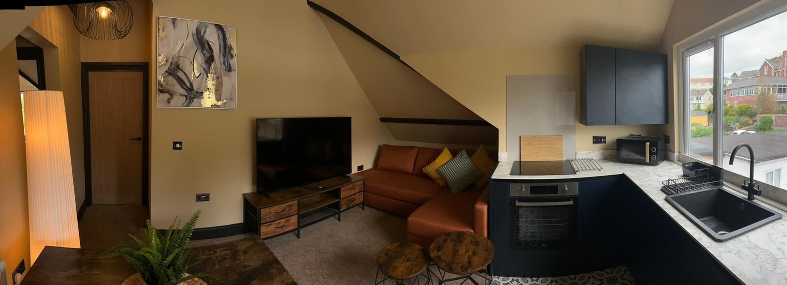 A modern apartment with a living room, kitchenette, and a large window.