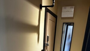 Un estrecho pasillo con piso alfombrado, una puerta con marco negro, una ventana con persianas y un aire acondicionado instalado en la pared.