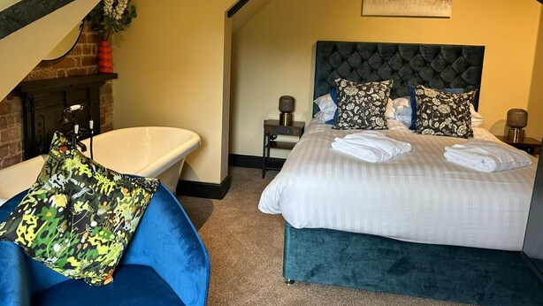 Un dormitorio con una cama grande, una bañera y una silla azul.