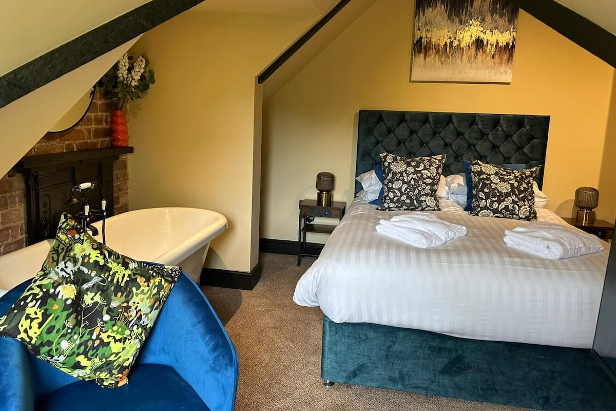 A bedroom with a large bed, a bathtub, and a blue chair.