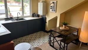 Una cocina compacta con ventana, un lavamanos, un tostador y una tetera. Hay una pequeña zona de comedor con una mesa y sillas.