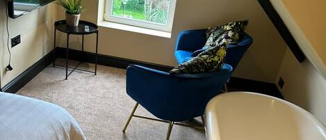 A bedroom with a large window, a blue chair, a white bathtub, and a bed.