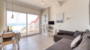 Ein modernes Wohnzimmer mit grauem Sofa, einem Esstisch mit Stühlen, einem Fernseher und einem großen Fenster mit Meerblick.