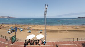Ein Strand mit Sonnenschirmen, Liegestühlen und Menschen.