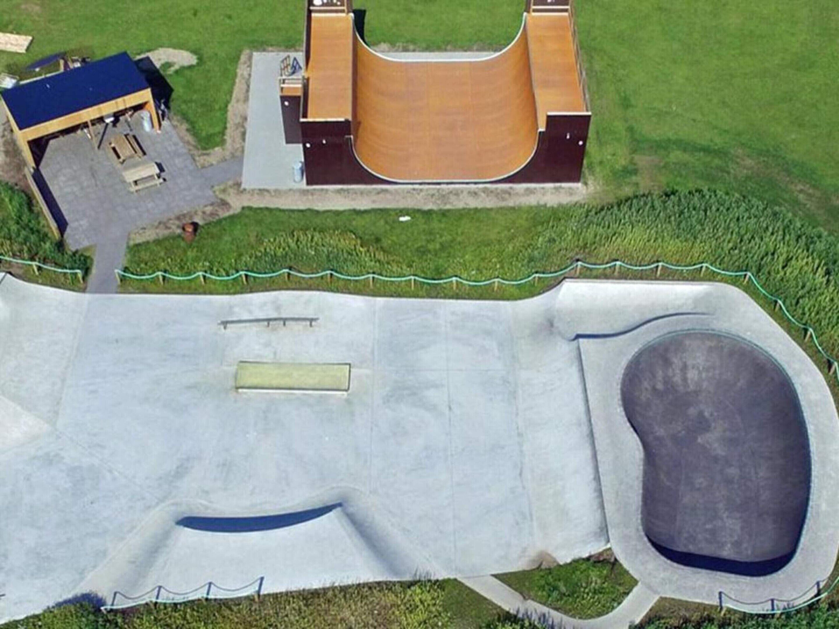 An aerial view of a park with a large wooden structure, a small building, and a concrete play area with a pool.