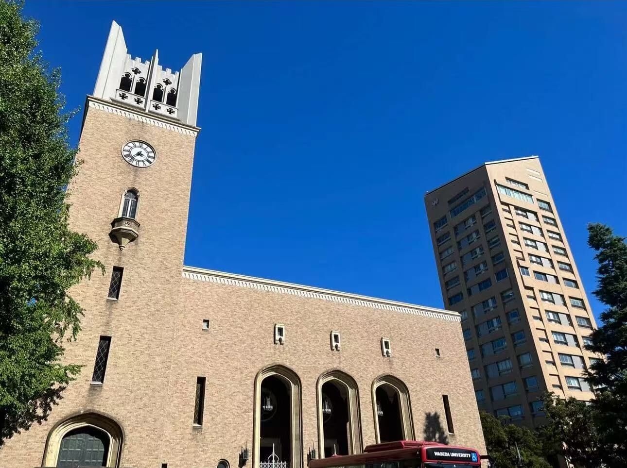A historic building with a clock tower and arched windows, adjacent to a modern high-rise building.