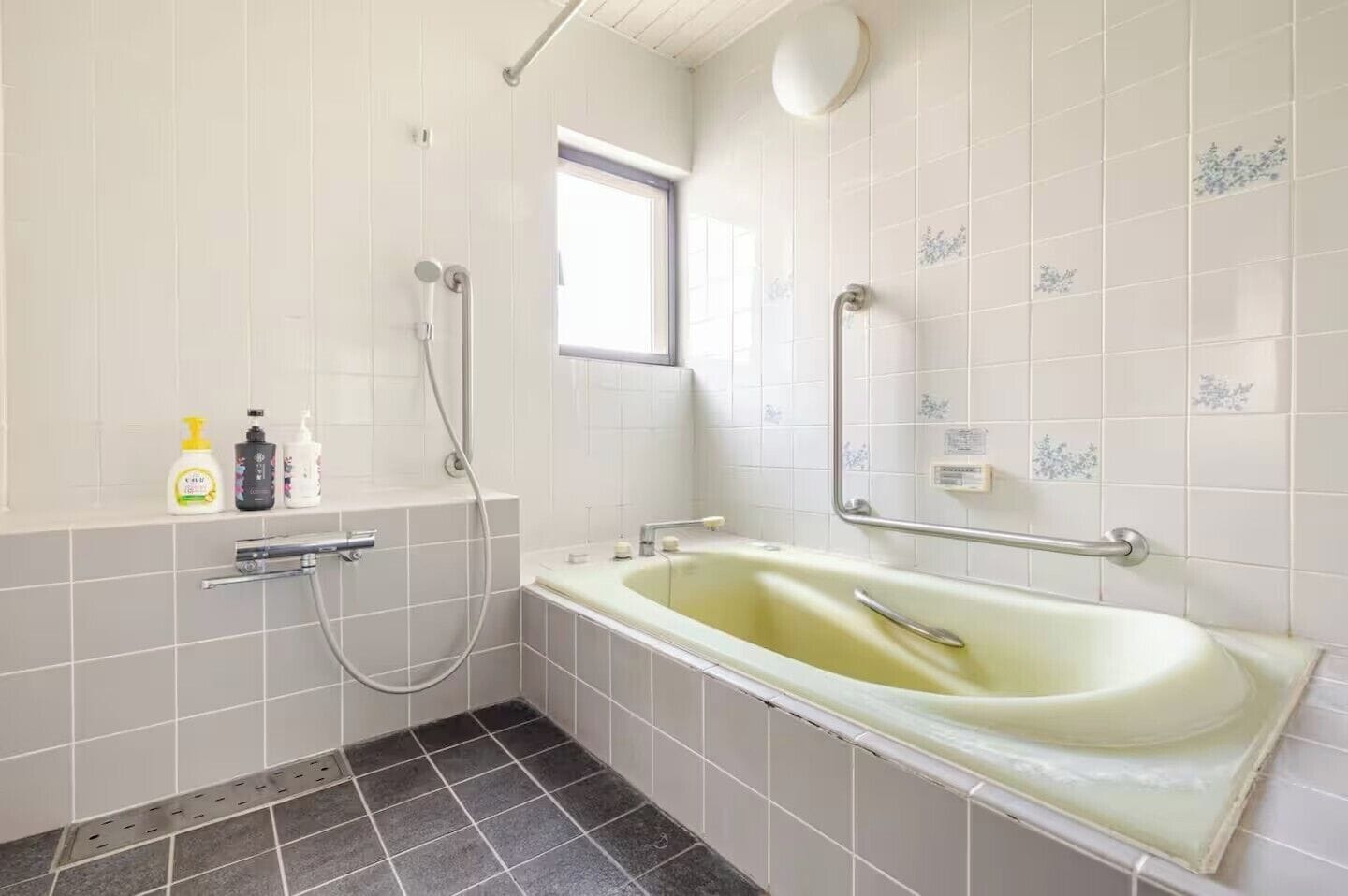 Ein Badezimmer mit einer Badewanne, einer Dusche und einem Fenster. Auf einem Regal befinden sich Toilettenartikel.