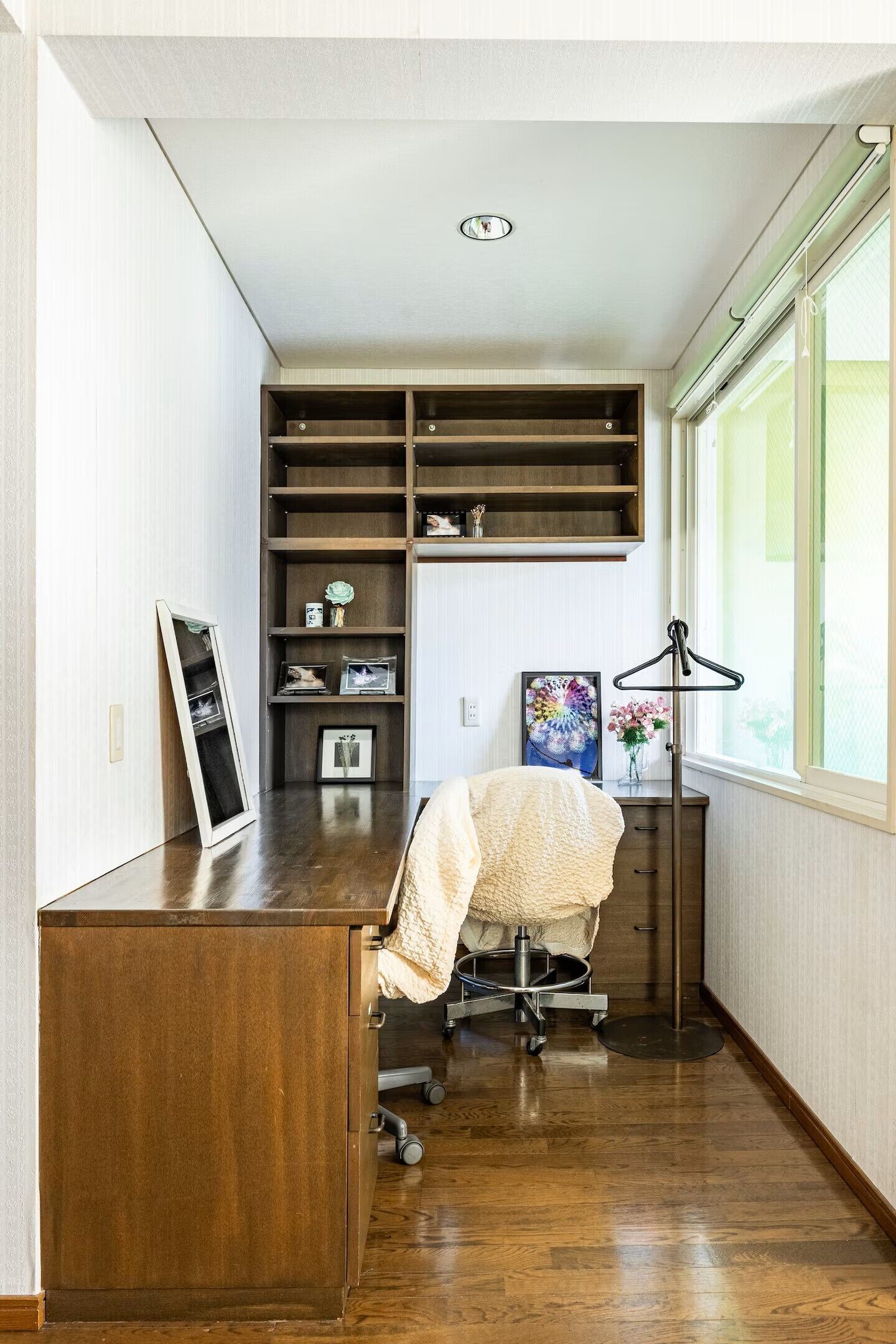 A room with a wooden desk, a chair, a hanging coat rack, and a window with blinds.