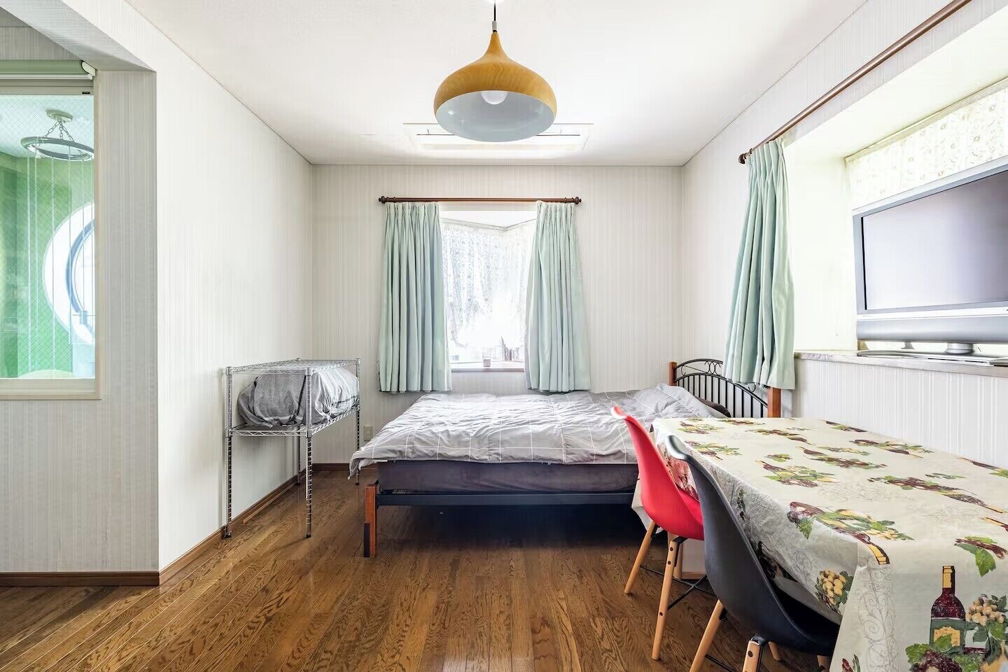 A bedroom with a bed, a desk with a chair, a TV, and a window with curtains.