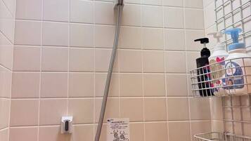 A shower with a handheld showerhead, a wall-mounted control panel, and a metal shelf with toiletries.