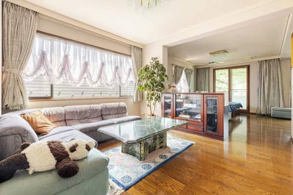 A spacious living room with a sofa, a glass coffee table, and a large window with curtains.
