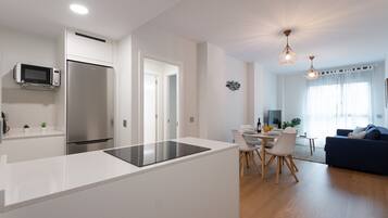 A modern kitchen with a built-in microwave and refrigerator, a dining area with a table and chairs, and a living room with a sofa and a blue couch.