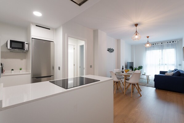 A modern kitchen with a built-in microwave and refrigerator, a dining area with a table and chairs, and a living room with a sofa and a blue couch.