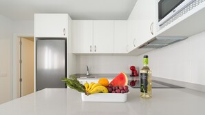A kitchen with white cabinets, a stainless steel refrigerator, a microwave, and a fruit bowl with bananas, grapes, and a watermelon.