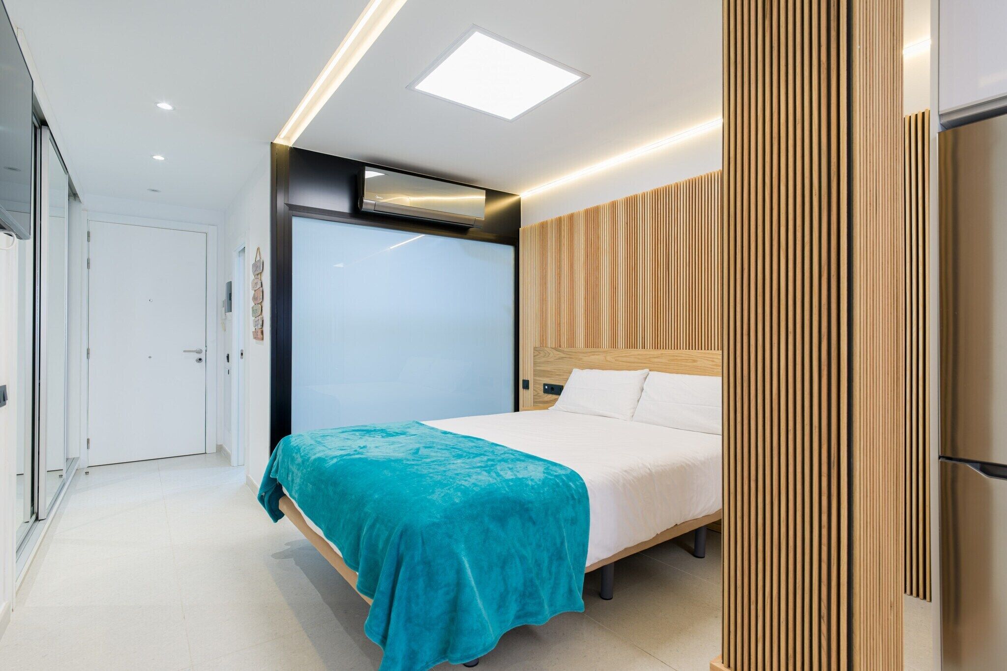 Quarto moderno com cama, cabeceira de madeira e colcha verde-água.